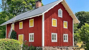 A red wooden house with a stone foundation, multiple windows, and a ladder leaning against it. - 5 Person Holiday Home in Valdemarsvik (Valdemarsvik)