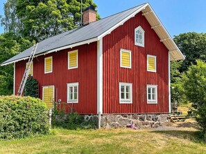 A red wooden house with a stone foundation, a ladder, and a clear sky.