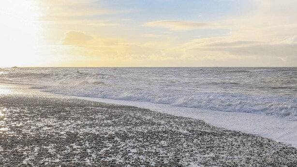 Een strand met golven en een heldere lucht.