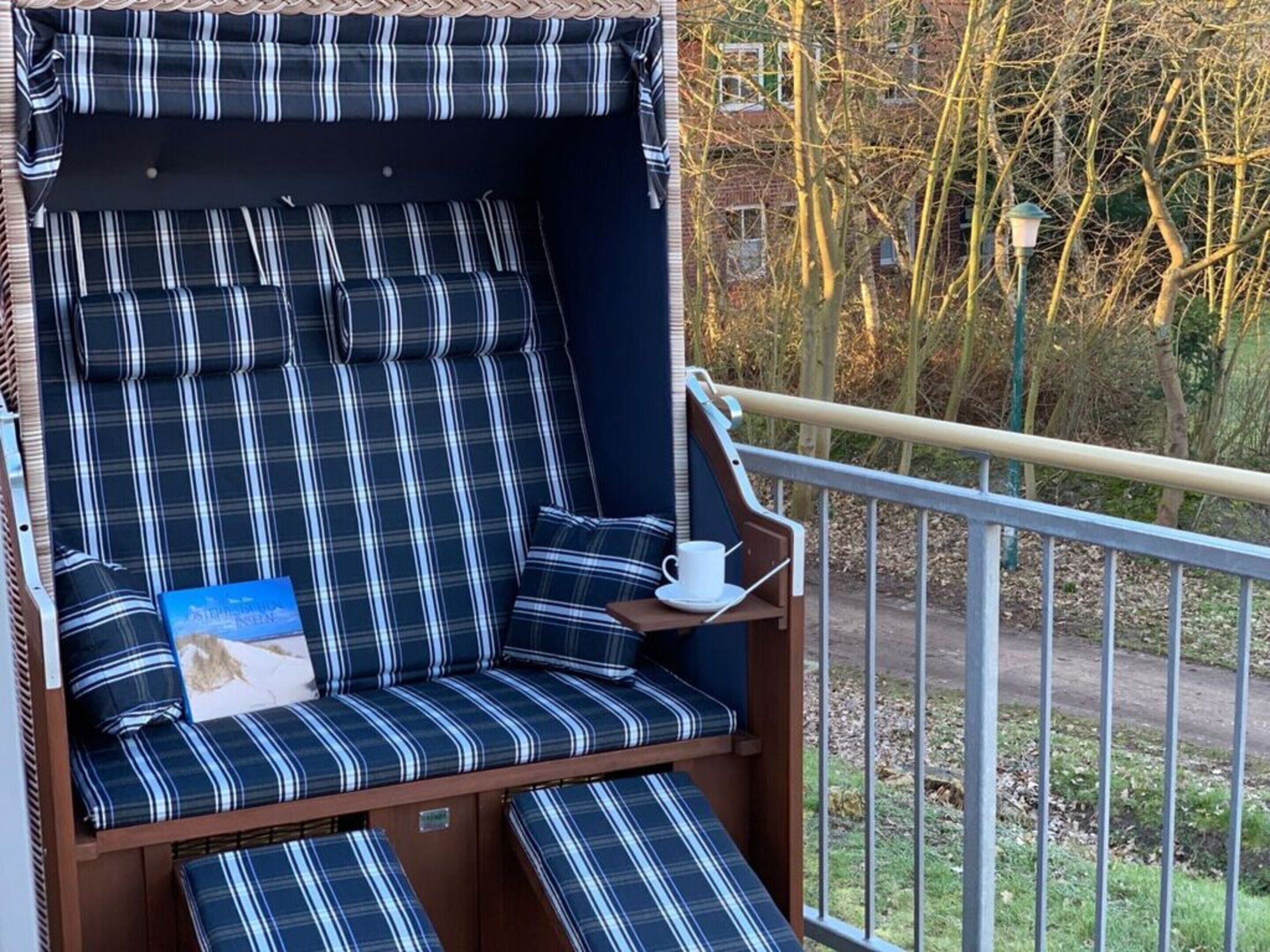 A balcony with a blue and white striped chair, a small table with a cup and saucer, and a book.
