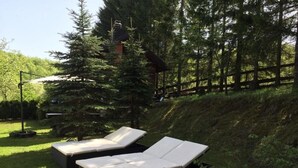 Dos sillones de exterior con cojines, ubicados en una pendiente cubierta de césped, con una valla de madera y árboles al fondo.