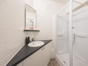 Une salle de bain moderne avec un lavabo blanc, un plan de toilette foncé et une cabine de douche en verre.