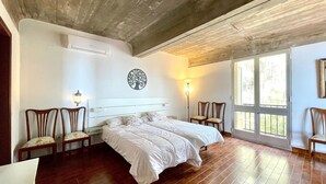 Een slaapkamer met een groot bed, twee stoelen, een wandlamp en een raam met uitzicht.