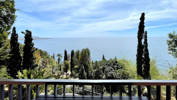 Een balkon met uitzicht op de zee en omliggende bomen.