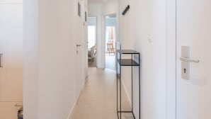 Un couloir aux murs blancs, une étagère en métal noir et une porte dotée d’un trou de serrure.