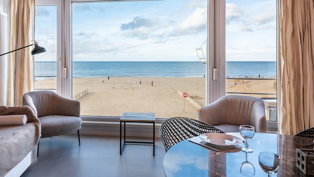 Une pièce dotée d’une grande fenêtre donnant sur une plage, une table avec des verres et deux chaises.