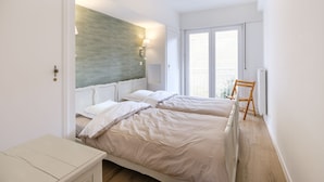 Une chambre moderne avec deux lits, un plancher en bois, un radiateur et une vue sur l’extérieur grâce à de grandes fenêtres.