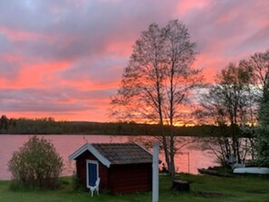 A small wooden cabin with a door and a window, surrounded by trees and a body of water. - 3 Person Holiday Home in Grangarde (Grangarde)