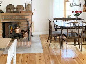 A room with a brick fireplace, wooden dining table, chairs, and a vase with flowers. - 3 Person Holiday Home in Grangarde (Grangarde)