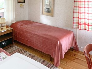 A single bed with a pink bedspread in a room with a wooden floor, a small desk with a lamp, and a chair. - 3 Person Holiday Home in Grangarde (Grangarde)