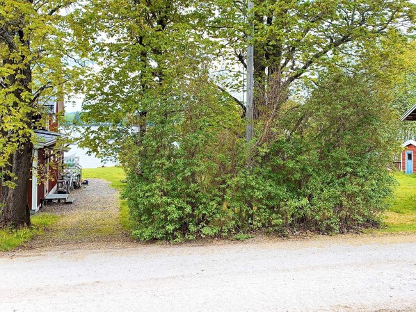 A gravel path leading to a rustic building with a blue door, surrounded by dense greenery and a body of water in the background. - 3 Person Holiday Home in Grangarde (Grangarde)