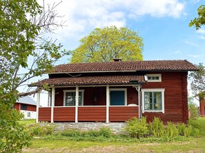 A red wooden house with a porch, a stone foundation, and a large tree in the background. - 3 Person Holiday Home in Grangarde (Grangarde)