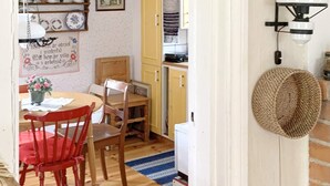 Un comedor con sillas de madera y una mesa, una cocina con armarios amarillos y una cesta tejida en la pared.