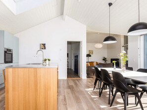 A modern kitchen with a wooden island, a dining area with black chairs, and a large window. - 5 Star Holiday Home in Albaek (Aalbaek)