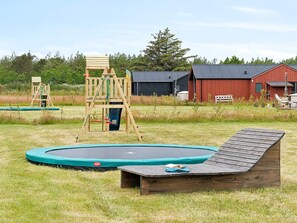 A playground with a wooden swing set and a trampoline in a grassy field. - 5 Star Holiday Home in Albaek (Aalbaek)