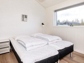 A bedroom with a bed, a bedside table, a wall-mounted lamp, and a window with a view of the outside. - 5 Star Holiday Home in Albaek (Aalbaek)