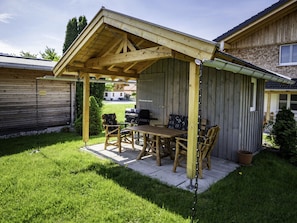 En overdækket terrasse med et træbord og stole, en grill og en potteplante.