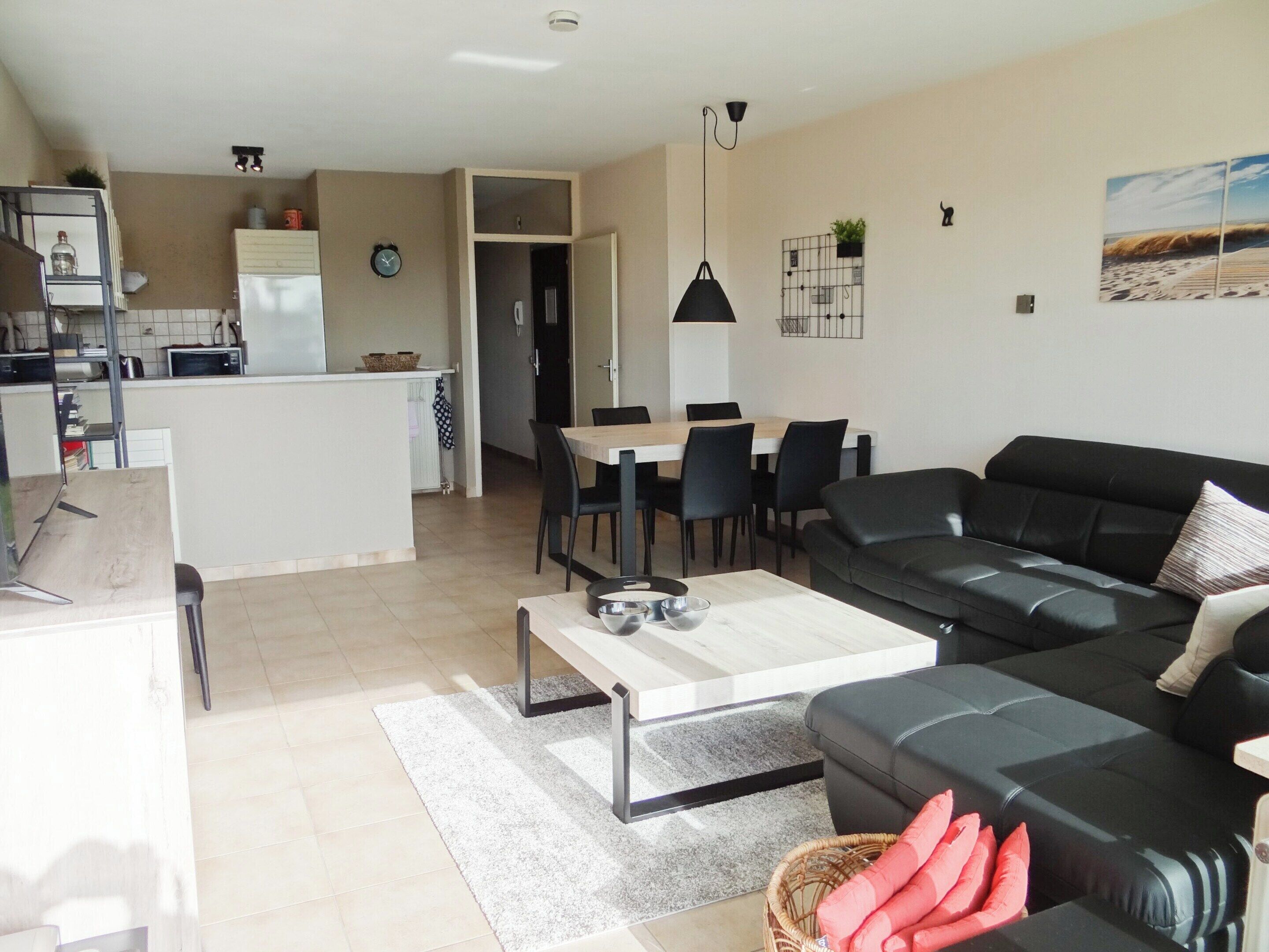 A modern living room with a black leather sofa, a wooden coffee table, and a dining area with a table and chairs.