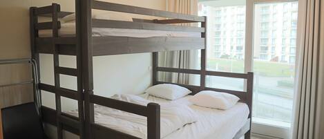 Una cama litera con ropa de cama blanca, una silla y una ventana con cortinas.