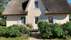 Ein zweistöckiges Haus mit Strohdach, weißen Außenwänden und einer kleinen Veranda.