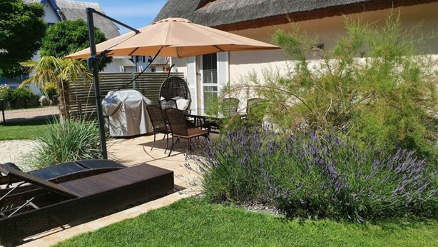 Ein Patio mit Grill, Sitzgelegenheit und einem Gebäude mit einem Reetdach.