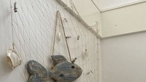Ein Netz mit einer Fischskulptur und einer Muschel an einer weißen Wand.