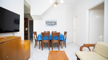 Uma sala de jantar com uma mesa posta para quatro pessoas, uma televisão à esquerda e um quadro sobre a mesa.