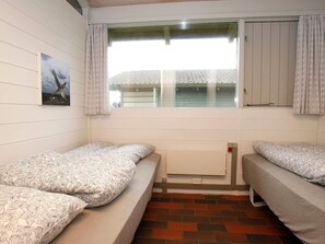 A small, single-room accommodation with two single beds, a window with curtains, a radiator, and a picture on the wall.