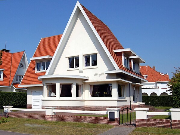 Ein modernes, zweistöckiges Haus mit rotem Ziegeldach, weißen Außenwänden und einem Backsteinfundament.