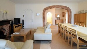 Un salon doté d’une cheminée, d’un téléviseur et d’un coin repas, avec une arche en briques donnant sur la cuisine.