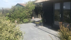 A modern building with a thatched roof, surrounded by lush greenery and a paved pathway leading to a glass door entrance. - Holiday Apartment Salt and Dunes (Schoorl)