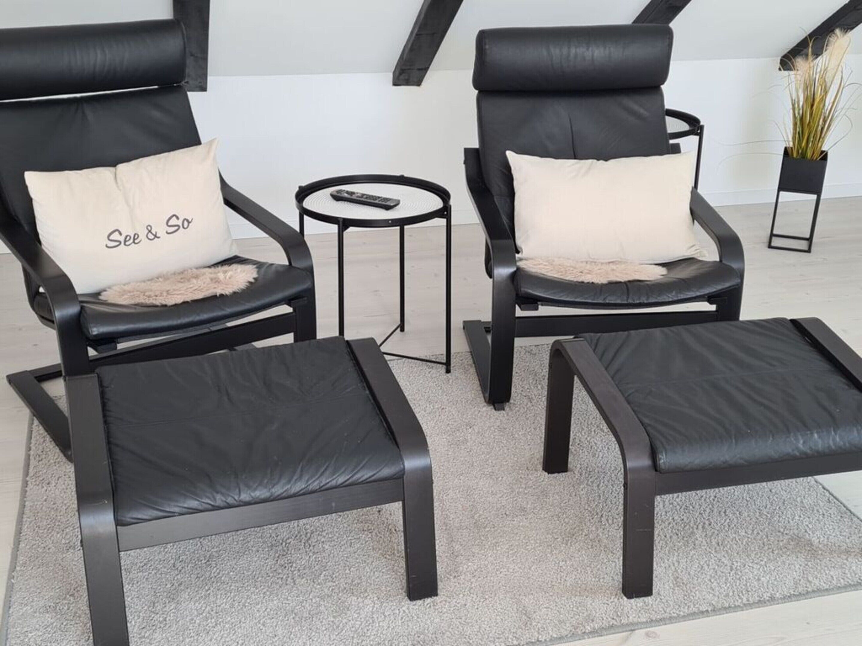 Two black leather armchairs with matching cushions, a small round side table, and a matching ottoman.