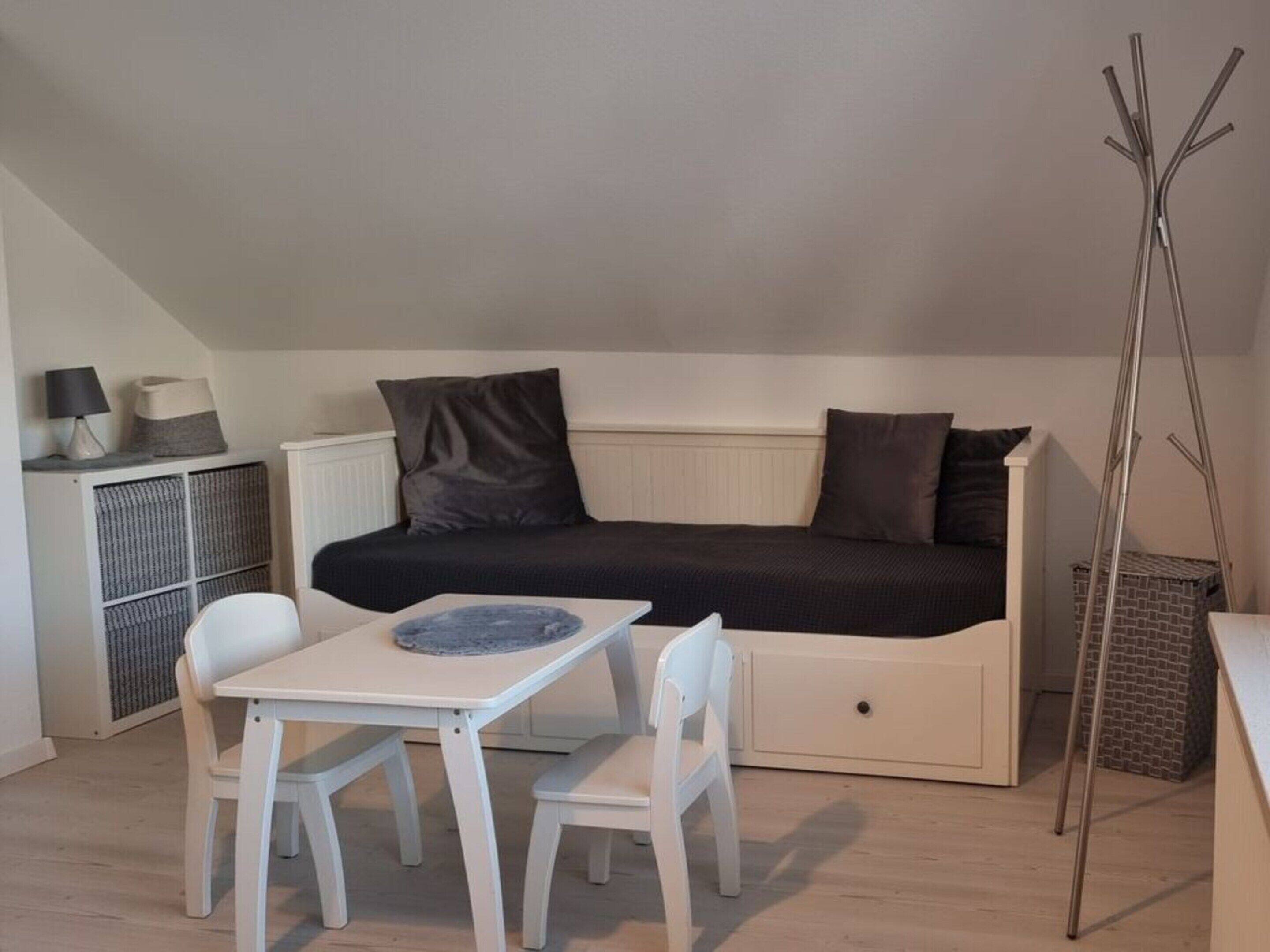 A small, cozy room with a bed, a table with two chairs, a radiator, and a ladder.