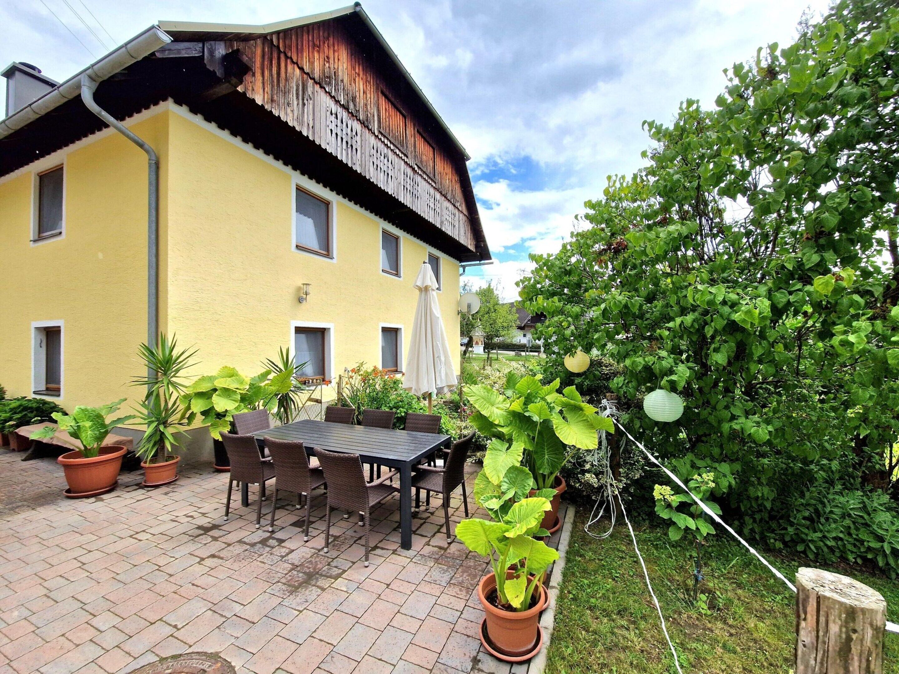 A yellow building with a balcony, potted plants, and a table with chairs in the courtyard.