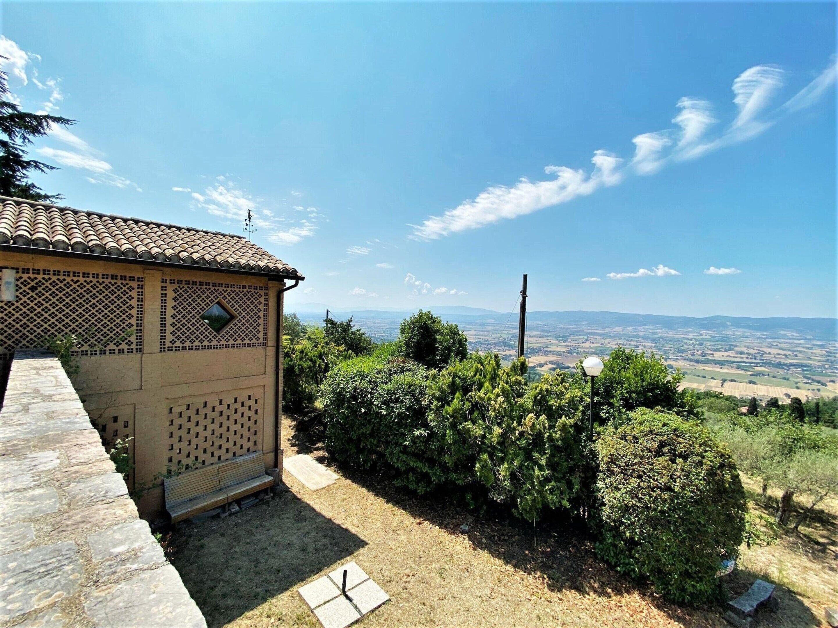 A rustic building with a tiled roof and lattice design, surrounded by greenery and a clear view of distant hills.
