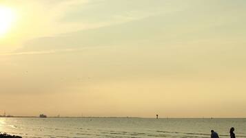 A beach scene with two people walking along the shore, a ship in the distance, and a clear sky.