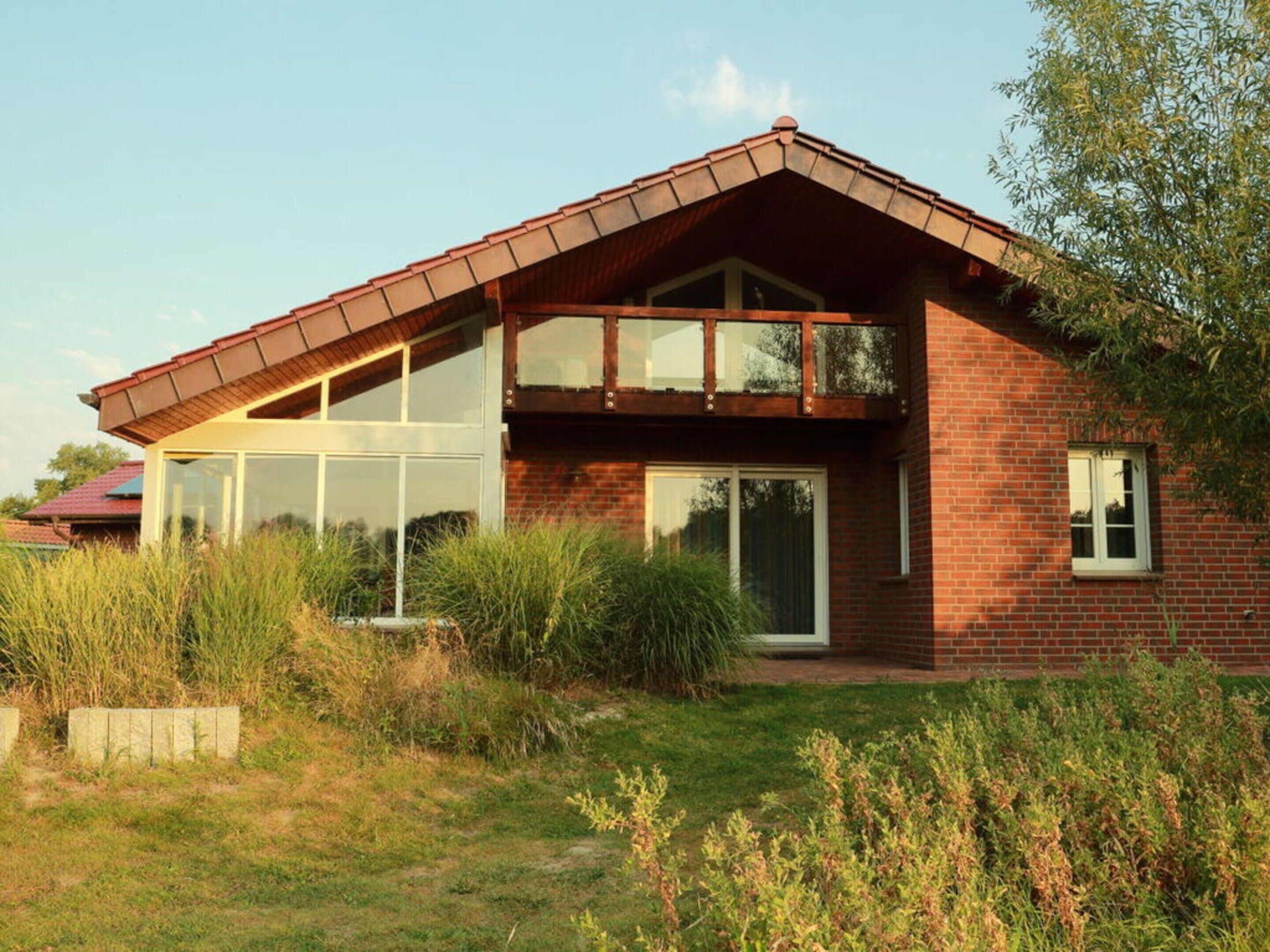 A modern two-story house with a sloped roof, large windows, and a brick exterior.