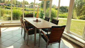 Un coin repas lumineux, avec une table et des chaises, de grandes fenêtres donnant sur un jardin et des maisons.