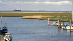 Un port de plaisance avec des bateaux amarrés, un navire à l’horizon et une zone herbeuse au premier plan.