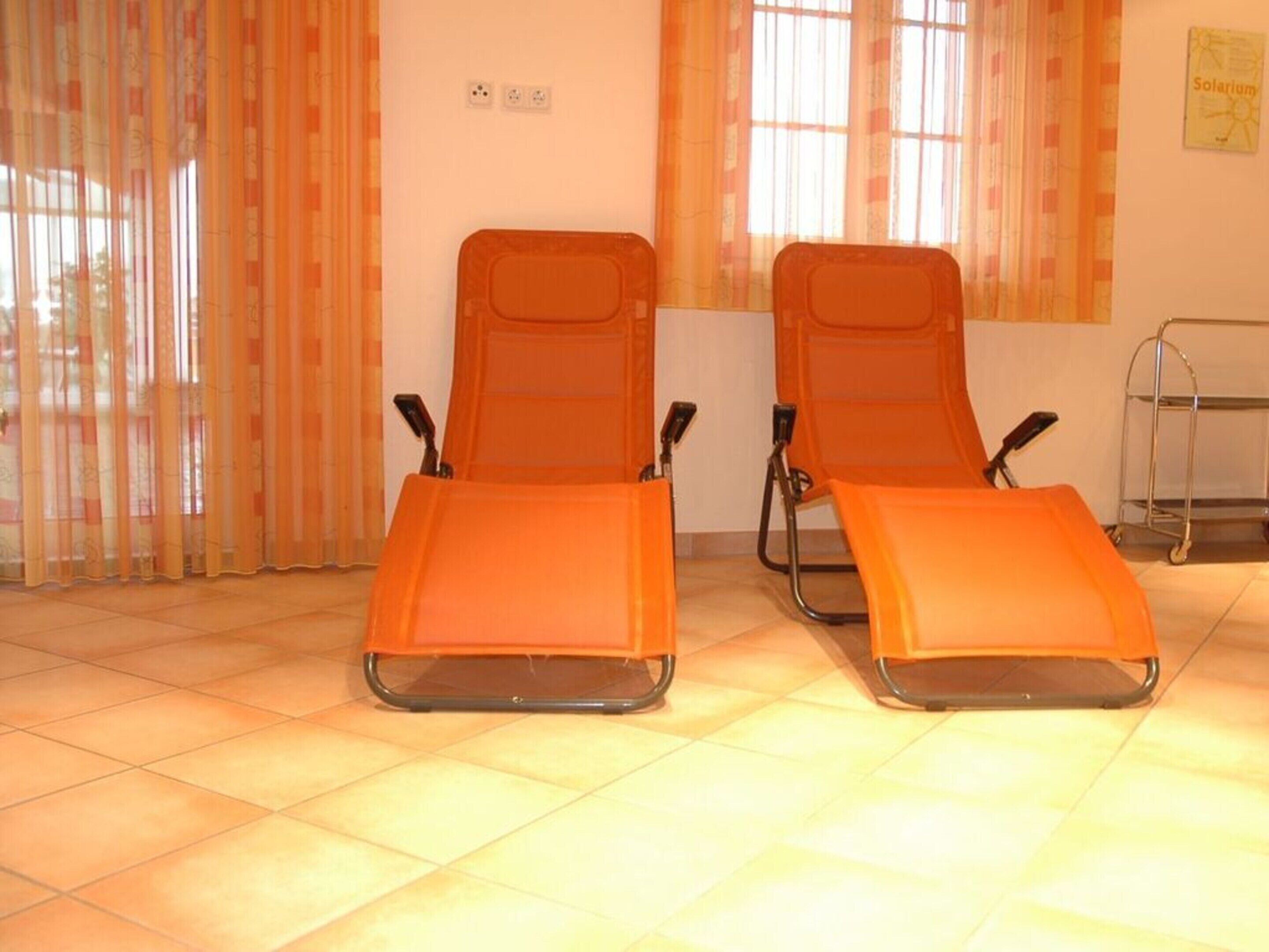 Two orange reclining chairs in a room with tiled flooring and a window with orange curtains.