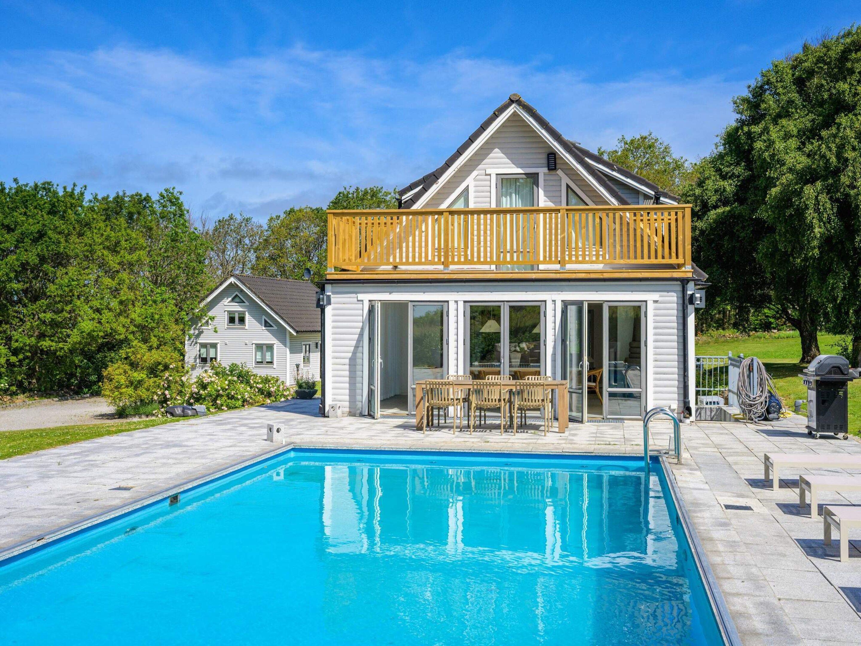 A house with a pool, a wooden deck, and a glass-enclosed patio.