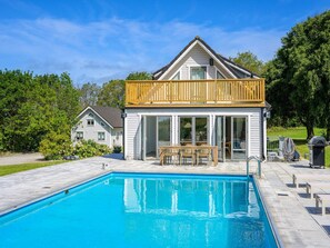 Une maison avec une piscine, une terrasse en bois et un patio fermé par des baies vitrées.