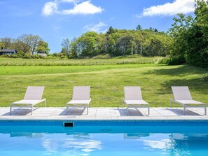 Une piscine bordée de quatre chaises longues alignées.