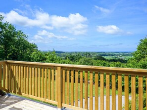 A wooden deck with a view of a green landscape and distant hills.