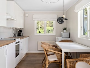 A compact kitchen with white cabinets, a built-in oven, a microwave, and a dining area with wicker chairs. - 5 Star Holiday Home in Bastad (Bastad)