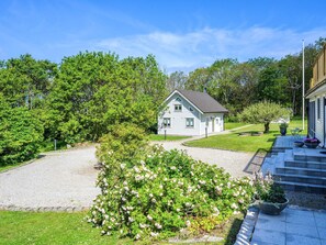 A single-story house with a gravel driveway, surrounded by lush greenery and a well-maintained lawn.