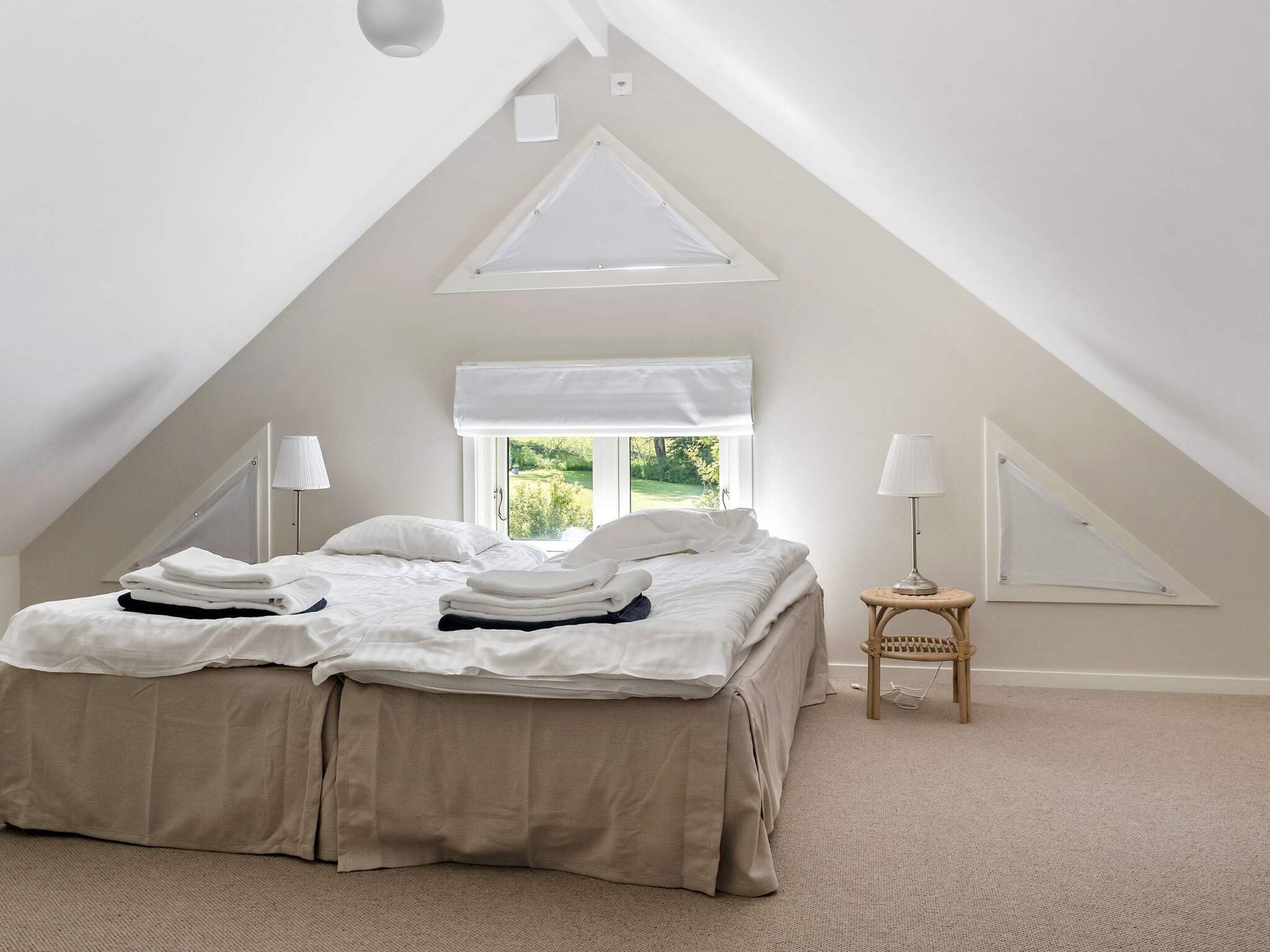 A bedroom with a bed, two bedside tables, a window with a view, and a sloped ceiling.