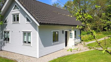A two-story house with a sloped roof, a gravel driveway, and a grassy yard.