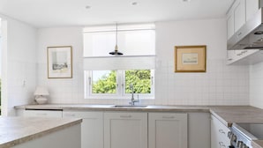 A modern kitchen with white cabinetry, a window with a view of greenery, and a pendant light. - 5 Star Holiday Home in Bastad (Bastad)
