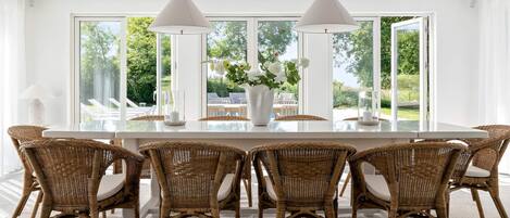 A dining area with a large table, wicker chairs, and pendant lights.